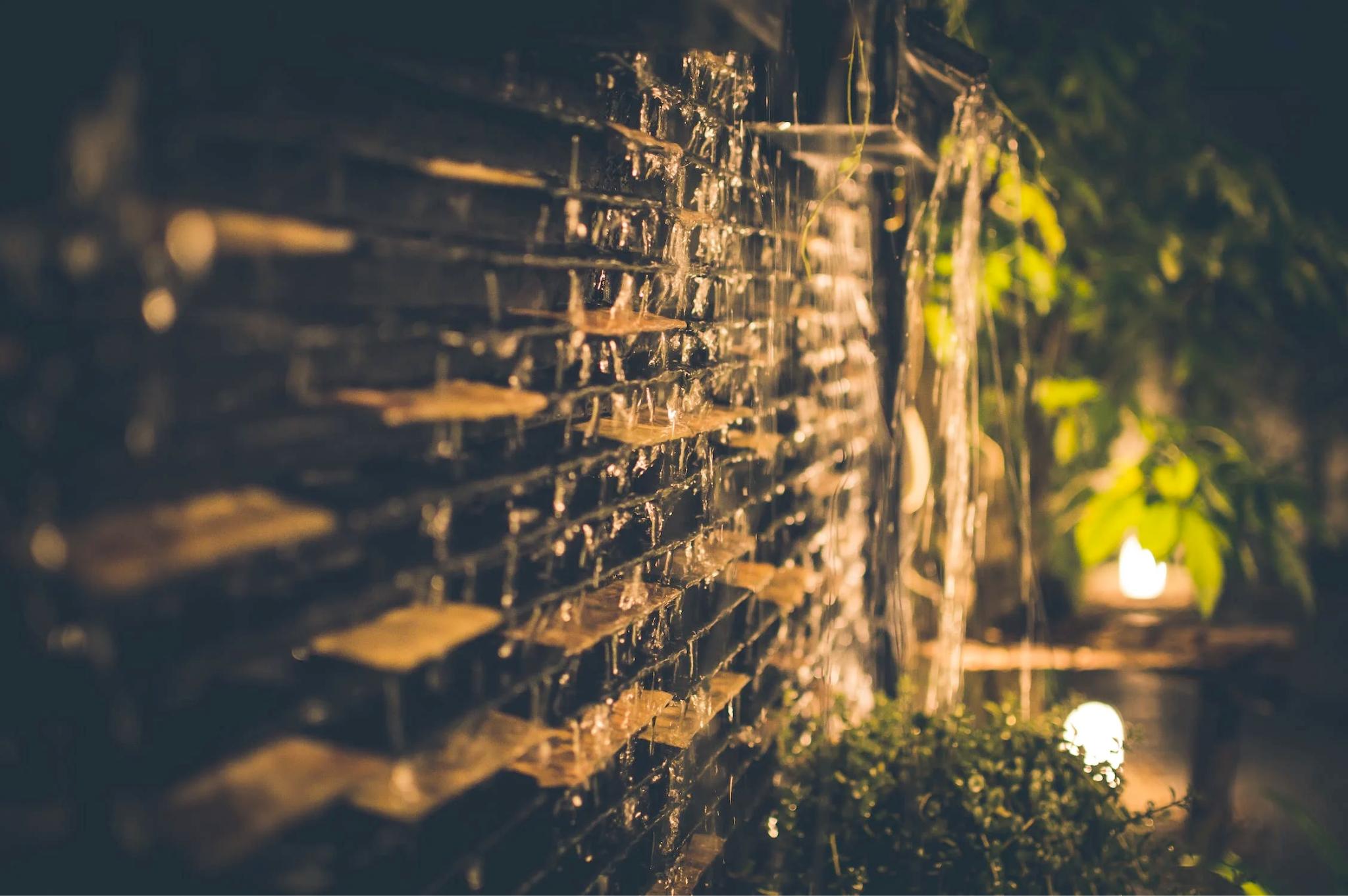 An image of outdoor lighting highlighting a water wall in the garden