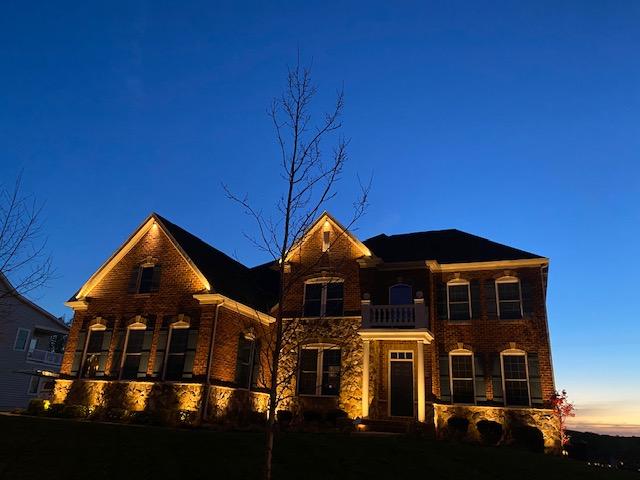 A beautifully lit residential home with outdoor lighting showcasing pathways, trees, and architectural features