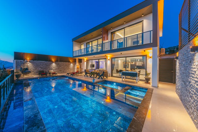 A beautiful villa with a large pool illuminated by warm landscape lighting