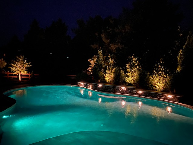 Warm landscape lighting reflecting off the pool water at night.
